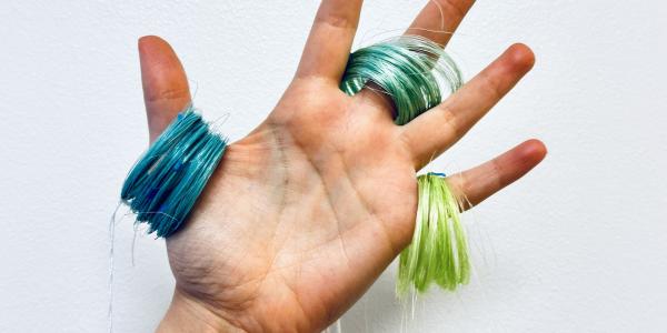 Hand holds three coils of thread in blue, green and neon green