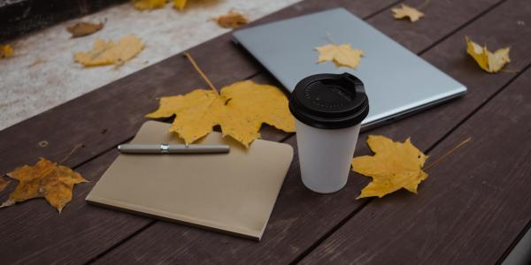 notebook, laptop and a coffee cup on a table with fallen leaves