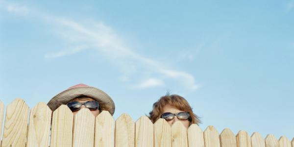 two people peek over a neighbor's fence