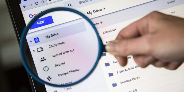 person holding a magnifying glass up to Google Drive screen on laptop