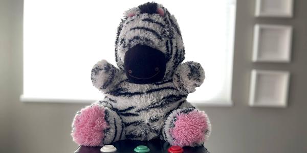 A stuffed zebra toy sits on a box with buttons