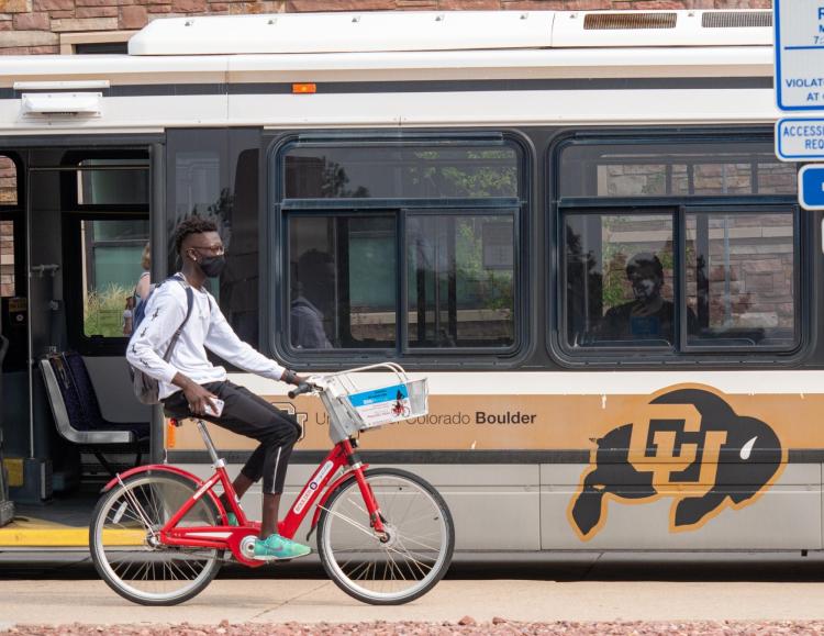 Student riding bike past a Buff Bus on campus