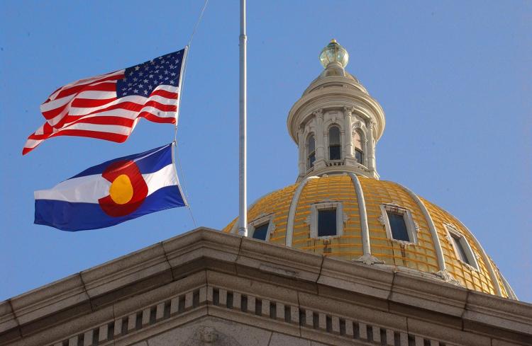 The American flag and the Colorado flag blowing in front of the state capitol dome.