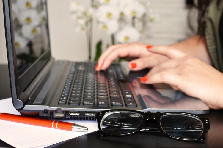 Person typing on computer, with pen and glasses nearby