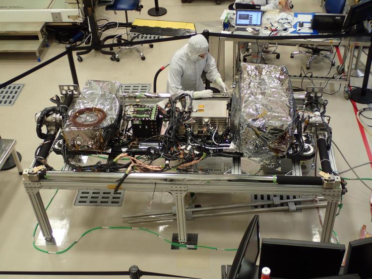 Technician in a clean room "bunny suit" and mask works on an array of machinery covered in silver foil