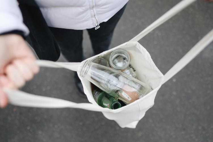 Person carrying empty glass bottles in a reusable bag