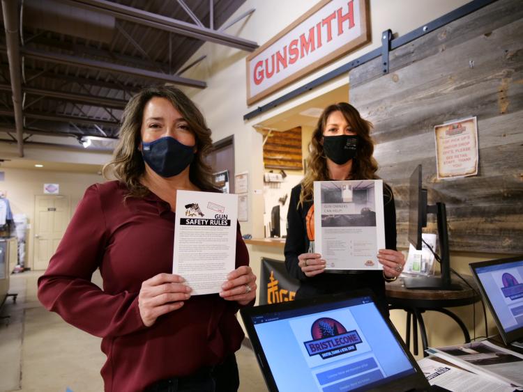 Two women hold up educational materials near a cash register