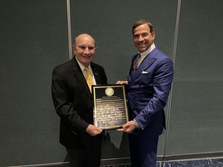 Ken Montera, right, presents Philip DiStefano, left, with a chancellor emeritus plaque designed with a black background, gold script and a gold university seal. 