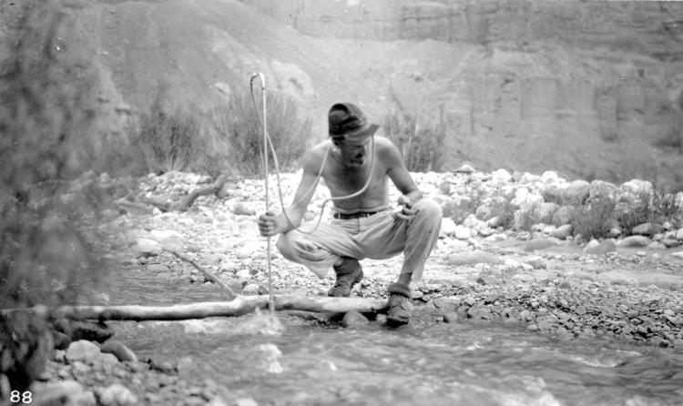 Man holding pole crouches in stream