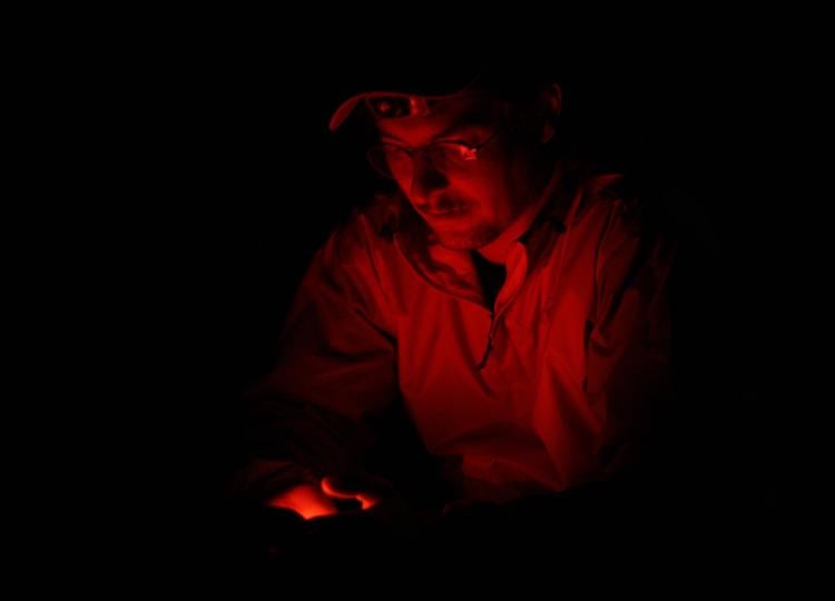 A red light illuminates a man wearing a cap in the dark