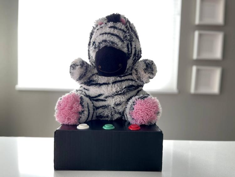 A stuffed zebra toy sits on a box with buttons
