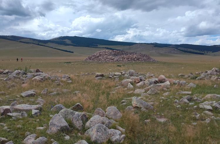 Grassy plain strewn with boulders with a large mound made of piled rocks