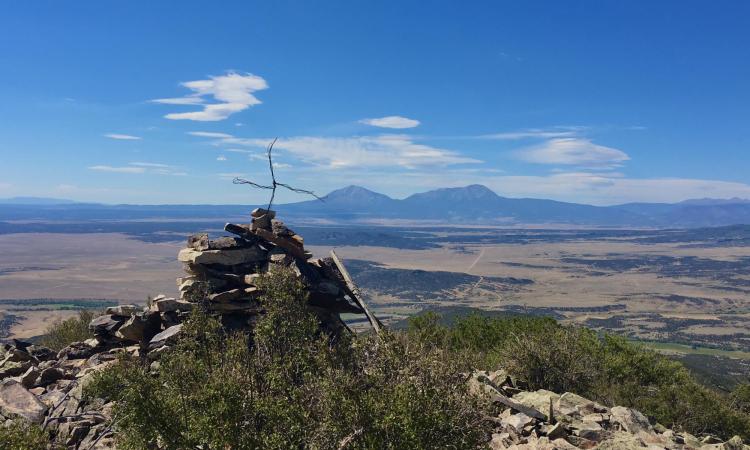 A cross made from metal wires sticks out from a pile of rocks on top of a mountain