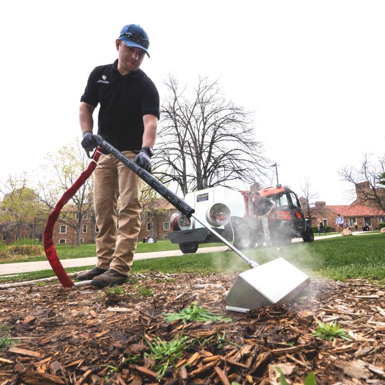 Grounds technician Pedro Vasquez uses a machine that provides hot steam to safely kill weeds
