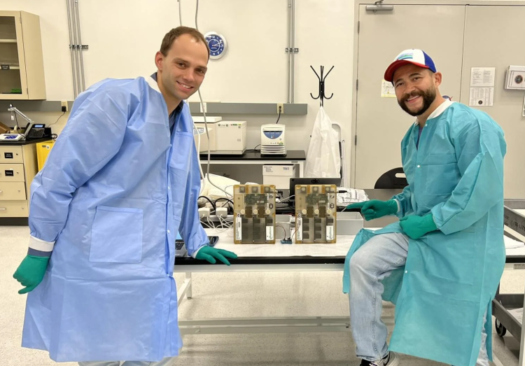 Tobias Niederwieser and Luis Zea pose by two cases on a table in a lab