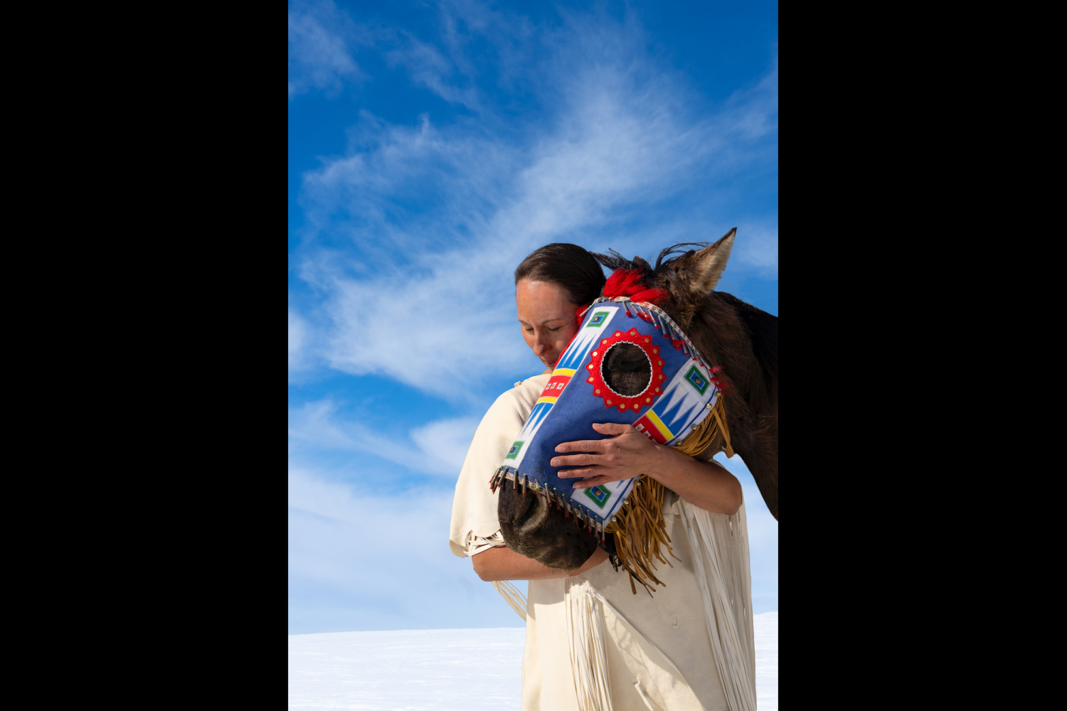 Woman stands with a horse wearing a colorful head covering
