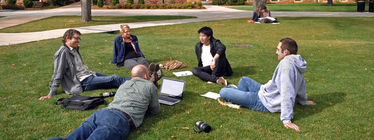 People sit in a circle on a campus lawn. 