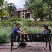 two students sit on a bench on campus, talking