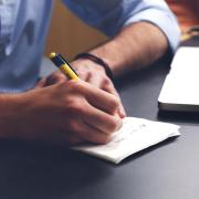 Person writes in notebook with laptop nearby