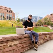 Student wearing mask working on laptop outside