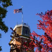 Flag flying atop Old Main building framed in red autumn leaves