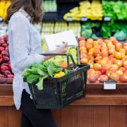 Person grocery shopping for produce with paper list in hand