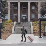 student with rolling suitcase departing campus for break