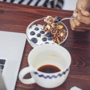 person eating yogurt with blueberries and granola while working on laptop