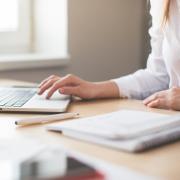 Woman works on laptop computer, with notebook and pen