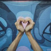 person making a heart with his hands in front of graffiti wall