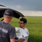Members of the CU Boulder flight crew working on a RAAVEN drone in 2019 during a mission with a tornado in the distance.