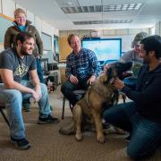 Engineering students and professor gathered around a big, fluffy dog in their laboratory