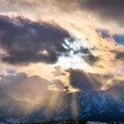 Sun peaks through clouds and snowy Flatirons