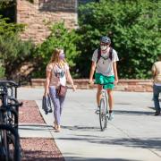Student riding a bike on campus, while a friend walks alongside him