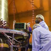 Engineers in cleanroom gear load a small satellite into a rocket