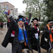 Graduates walk in commencement procession, some donning ski goggles in the snow