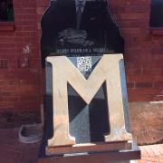 Gold letter M plaque with cutout of Nelson Mandela